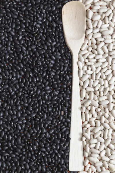 white beans and black beans separated by a wooden spoon. Black and white composition