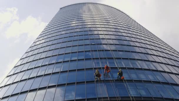 Három férfi, vörös és sötét munkaruhában, akik egy üzleti felhőkarcoló külső ablakait takarítják. — Stock videók