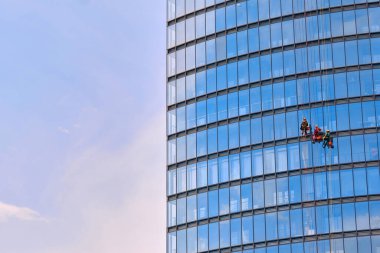 Kırmızı ve koyu renk iş kıyafetleri içindeki erkek işçiler bir iş gökdeleninin dış camlarını temizliyor - endüstriyel dağcılık
