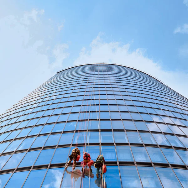 Tres hombres trabajadores en ropa de trabajo roja y oscura limpiando las ventanas exteriores, vista inferior. Exterior — Foto de Stock