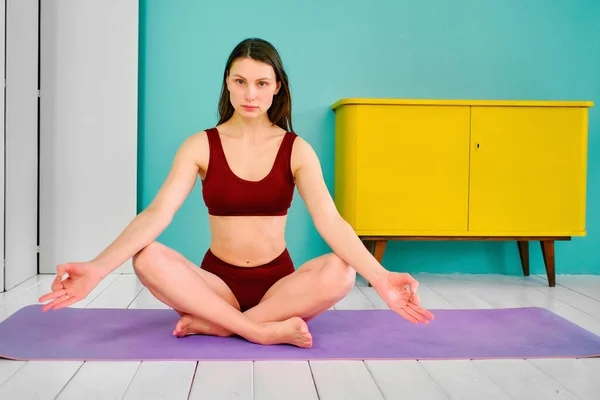young girl with open eyes in a sports uniform in a yoga pose sits on a purple rug