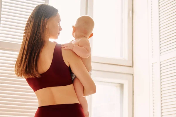 Mãe com um bebê em seus braços em um fundo de janela — Fotografia de Stock