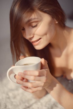 Elinde bir fincan çayla genç ve çekici bir kadın başka tarafa bakıyor ve gülümsüyor.