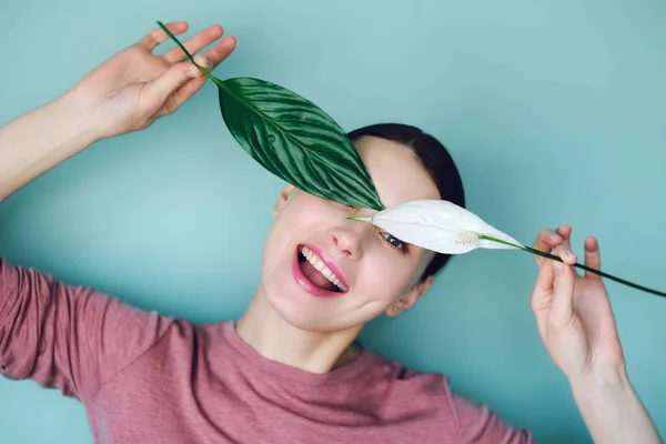 Niña sonriente con una camisa blanca con una flor en las manos sobre un fondo turquesa mirando a la cámara — Foto de Stock