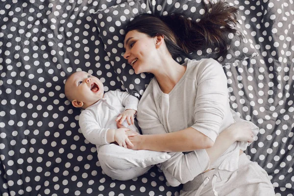 Uma jovem mãe sorridente brinca com o bebê em uma cama listrada — Fotografia de Stock