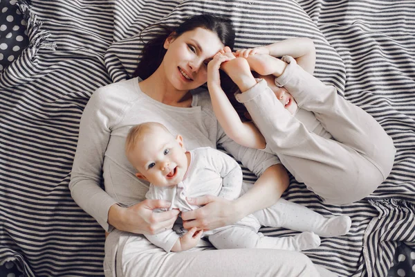 Mãe sorridente brinca com duas meninas em uma cama listrada. as crianças estão rindo — Fotografia de Stock