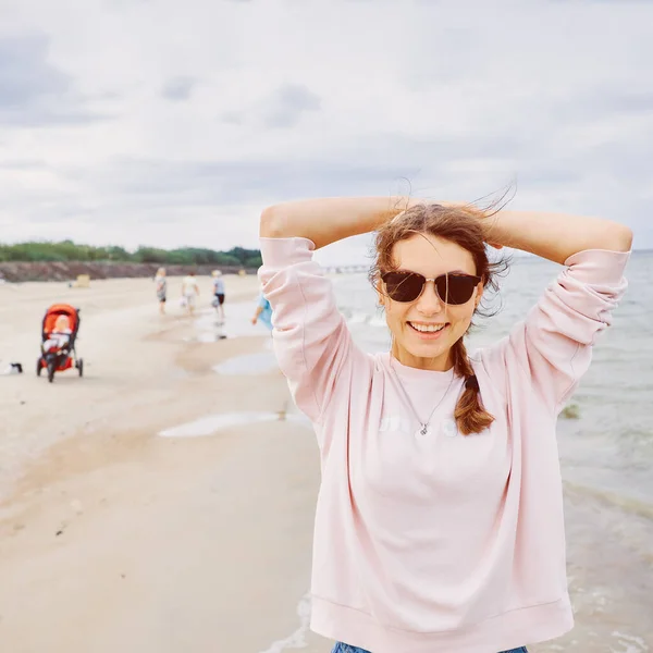 Portret uśmiechniętej dziewczyny w różowym swetrze na tle plaży — Zdjęcie stockowe