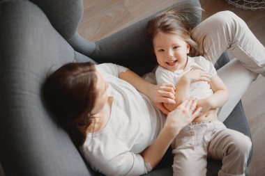 3 yaşında bir kızı olan anne gri bir koltukta oturur, sarılır ve güler.