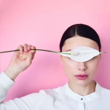 Pembe arka planda elinde çiçekle beyaz gömlekli bir kız.