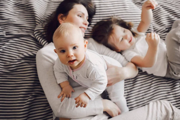 Leende mamma leker med två små flickor på en randig säng. barn skrattar — Stockfoto