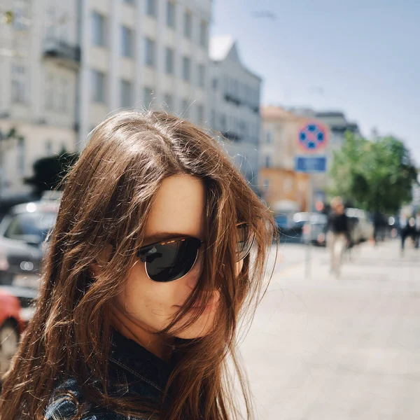 Portrait of a girl in sunglasses against the background of the city with flying hair in the wind — Stock Photo, Image