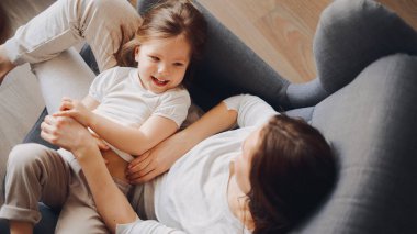 3 yaşında bir kızı olan anne gri bir koltukta oturur, sarılır ve güler.