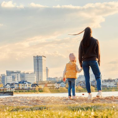 Anne ve kızı sırtlarını kumsala dayayıp şehrin manzarasına karşı duruyorlar.
