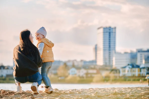 Mom and daughter are standing with their backs on the beach against the backdrop of the city landscape — Stock Photo, Image