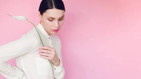 Girl in a white shirt with a flower in her hands on a pink background — Stock Photo, Image