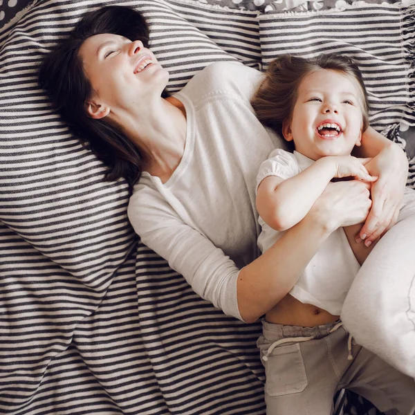 Bela mãe com 3 anos de idade filha abraçar e rir enquanto deitado na cama listrada — Fotografia de Stock