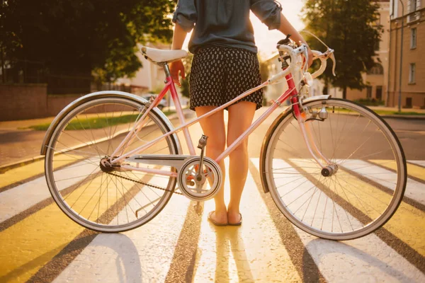 Flicka med en cykel på stadens bakgrund i solljuset, baksida vy — Stockfoto