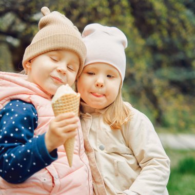 2 küçük kız. 3 yaşında. Parkta birlikte dondurma yiyorlar.