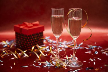 İki kadeh şampanya ve kırmızı arka planda konfeti ve yılan yağıyla birlikte hediye standı. Yeni yıl ve Noel için tebrik kartı. Romantik kartpostal.