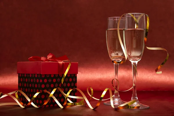 İki kadeh şampanya ve kırmızı arka planda konfeti ve yılan yağıyla birlikte hediye standı. Yeni yıl ve Noel için tebrik kartı. Romantik kartpostal.