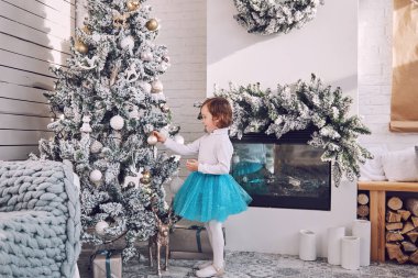 Küçük kız İskandinav tarzında bir odada Noel ağacı süsler. Yeni yıl kutlaması.
