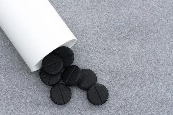 Aktivt kol tabletter för att rena kroppen spillt från en flaska på grå bakgrund. Top View närbild. Med plats för Text — Stockfoto
