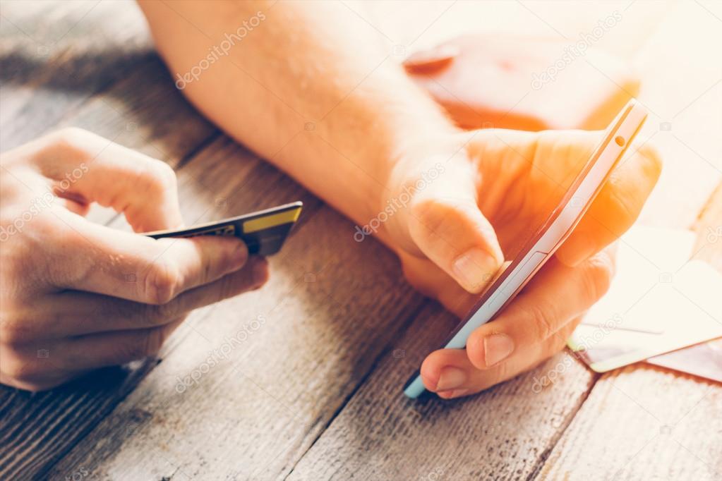 Man Hands holding credit card and using mobile phone in sunlight. Online shopping, online banking and online marketing. shallow depth of field, toning photo