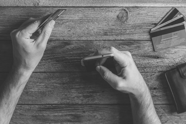 Man Hands holding credit card and using mobile phone. Online shopping, online banking and online marketing. top view,  black and white toning photo