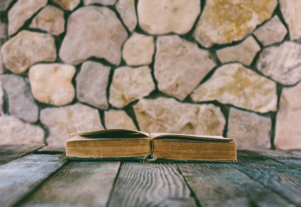 Otwarcie starej książki na starym drewnianym stole na tle ściany z kamienia. Selektywny fokus, tonowanie zdjęcie. z miejsca na tekst — Zdjęcie stockowe