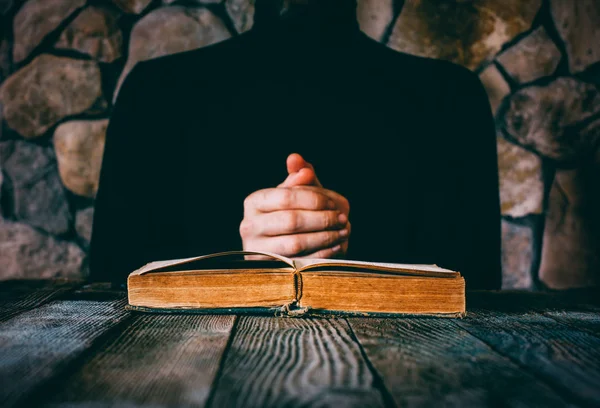 Masculino em roupas pretas na frente de um livro velho aberto. o conceito de oração, estudo, bruxaria. foco seletivo — Fotografia de Stock