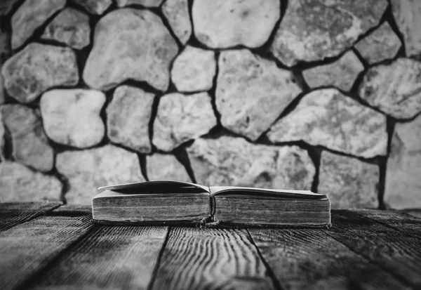 Otwarcie starej książki na starym drewnianym stole na tle ściany z kamienia. Selektywny fokus, czarna idealna białe zdjęcie. z miejsca na tekst — Zdjęcie stockowe