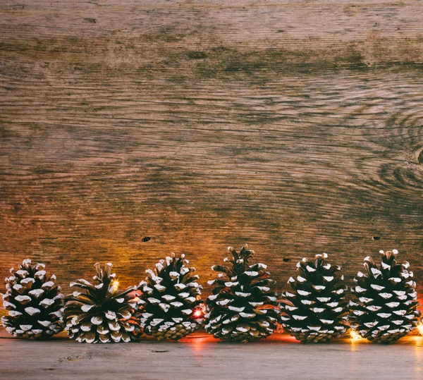 Feestelijke kerst achtergrond. Spar kegels en garland lichten in de oude schuur planken — Stockfoto