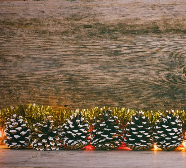 New Year's bakgrund. FIR kottar, gyllene glitter och garland lights i den gamla ladan boardsr. tonade foto — Stockfoto