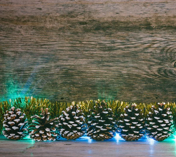 Fundo festivo de Natal. cones de abeto, ouropel dourado e luzes guirlanda em um celeiro velho placas. Foto matizada — Fotografia de Stock