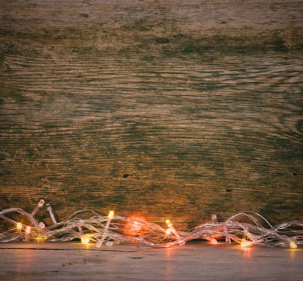 Feestelijke kerst achtergrond. Lichten garland op een oude schuur boards. Getinte foto — Stockfoto