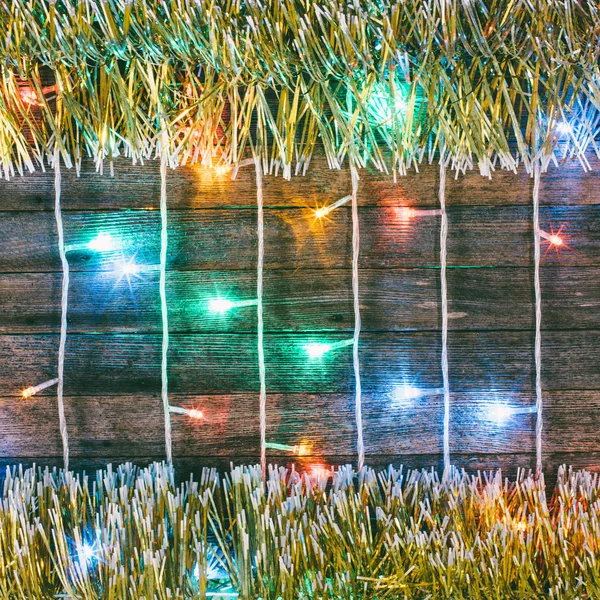 Świąteczny Bożego Narodzenia tło. Wielobarwny świateł girlanda i błyskotka złota na starych deskach stodoły. Przyciemnione zdjęcie — Zdjęcie stockowe