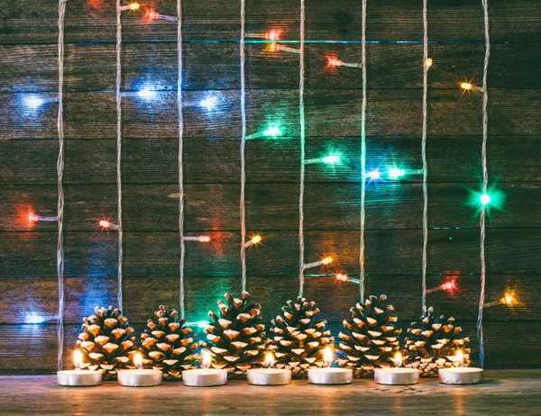 Festlig nyår och jul koncept. Mångfärgade lampor garland, fir kottar och ljus på bakgrunden av gamla ladugården styrelser. Toning foto — Stockfoto