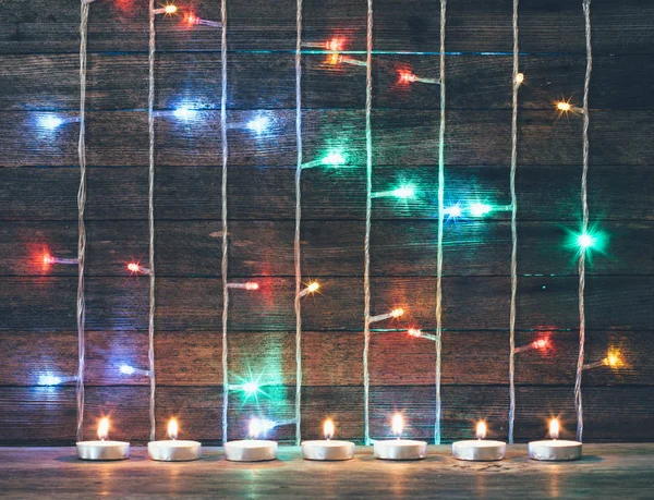 Festive Christmas, new year concept. Colored lights, garlands and candles on the background of old barn boards. Tinted photo — Stock Photo, Image