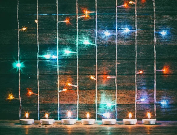 Festive Christmas, New Year concept. Multicolored lights garlands and candles on the background of old barn boards. Toning photo — Stock Photo, Image