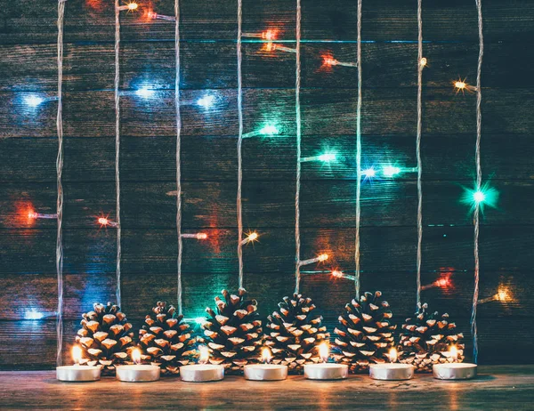 喜庆的圣诞，新年概念。五彩的灯光花环、 冷杉球果和旧谷仓板的背景上的蜡烛。调色的照片 — 图库照片