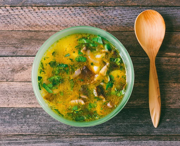 Sopa de champiñones con hierbas y una cuchara de madera en la vieja mesa de madera de cerca, vista superior. foto teñida — Foto de Stock