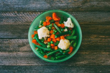 Asya mutfağı. havuç, bezelye, fasulye, karnabahar yukarıdan görmek eski ahşap masada yeşil plaka sebze karışımı. renkli fotoğraf