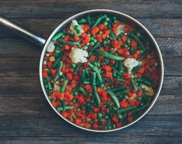 Asiatisches Gericht. Gemüsemischung aus Möhren, Erbsen, grünen Bohnen und Blumenkohl in der Pfanne auf einem alten Holztisch, Nahaufnahme von oben. getöntes Foto — Stockfoto