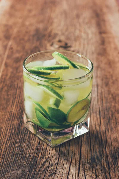 O coquetel Margarita com cubos de limão e gelo na velha mesa de madeira de perto, foto matizada — Fotografia de Stock