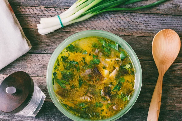 Pilzsuppe in einer Schüssel, Bund grüne Zwiebeln, Pfeffermühle und ein Holzlöffel auf einem alten Holztisch. Nahaufnahme von oben. getöntes Foto — Stockfoto