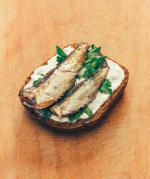 Sandwich of canned sprats on rye bread with mayonnaise and parsley, and dill on a wooden cutting board close up — Stock Photo, Image