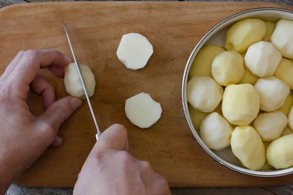 Uomo cuocere le fette di patate con un coltello da cucina su un tagliere. vista dall'alto primo piano — Foto Stock
