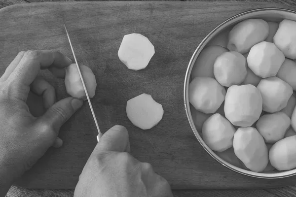 Uomo foto in bianco e nero cuocere le fette di patate con un coltello da cucina su un tagliere. vista dall'alto primo piano — Foto Stock