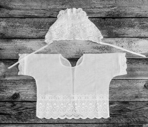 Cap and shirt for a newborn on the old rustic wooden table close-up view from above. black and white photo — Stock Photo, Image