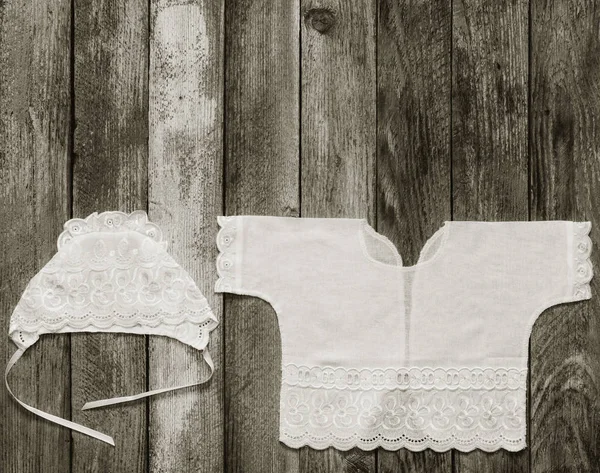 Foto en blanco y negro de una gorra y una camisa para un recién nacido en la vieja mesa rústica de madera vista de cerca desde arriba. con espacio para texto —  Fotos de Stock